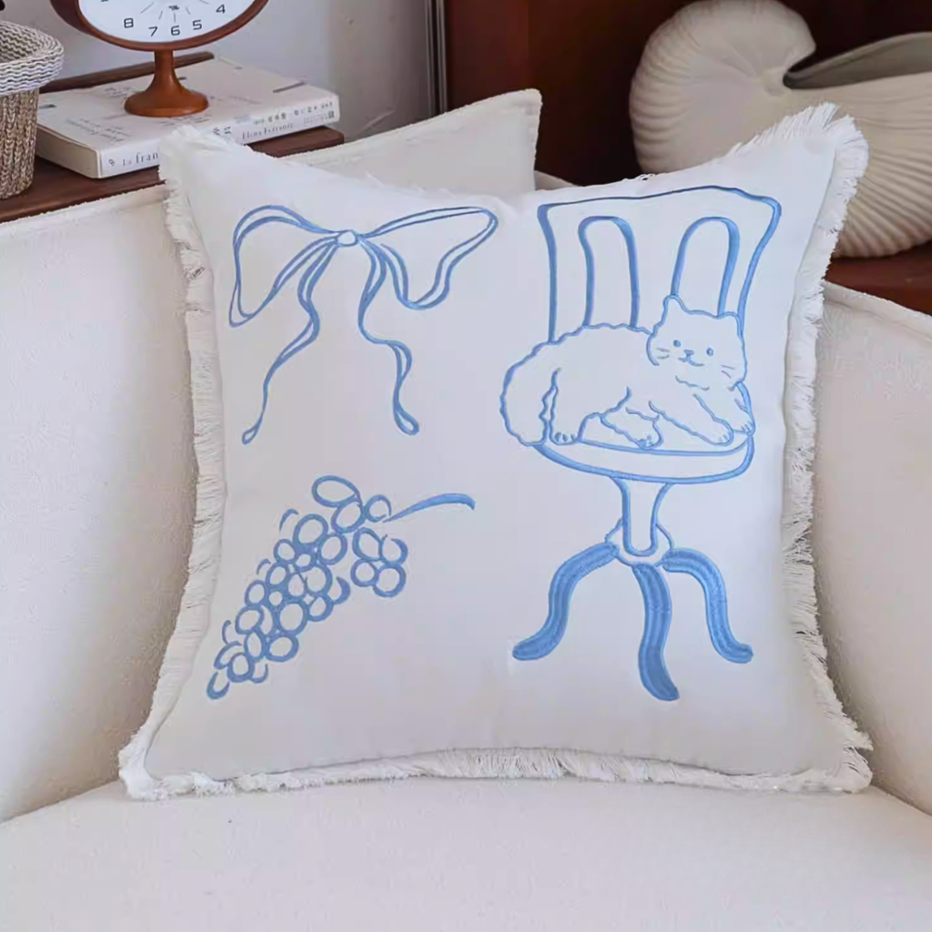 Decorative pillow with blue line art on a white background, placed on a couch.
